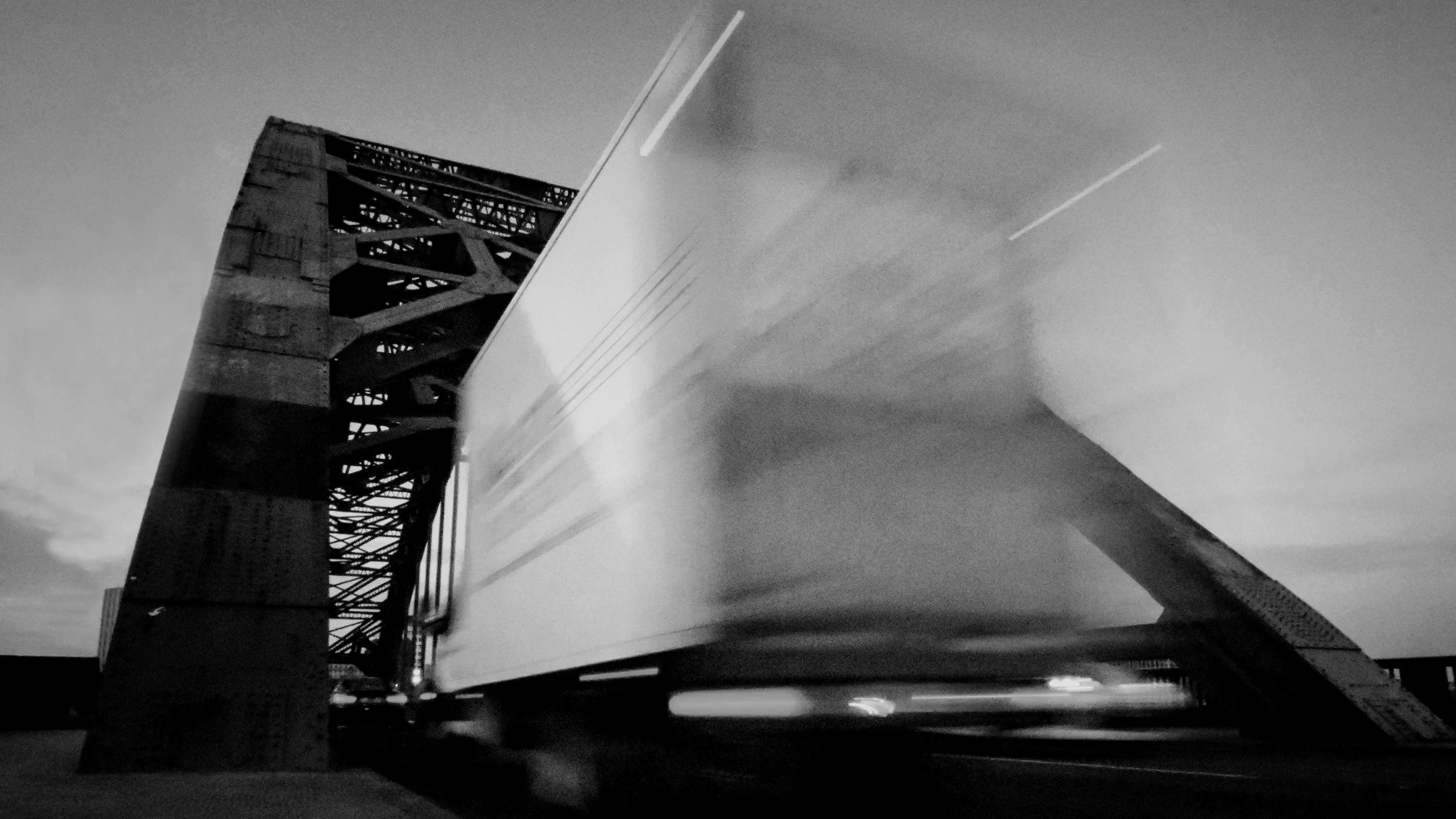 An articulated lorry crossing a steel bridge at dusk, blurred by its own speed